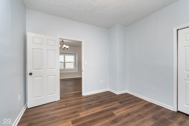 unfurnished room featuring dark hardwood / wood-style flooring, a chandelier, and a textured ceiling