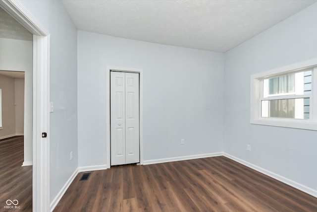 unfurnished bedroom with a textured ceiling, dark wood-type flooring, and a closet