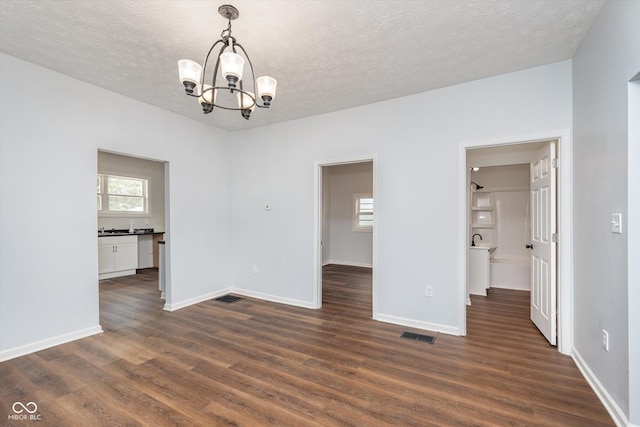 spare room featuring dark wood-type flooring, a chandelier, and a textured ceiling