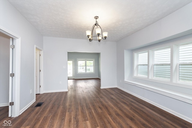 spare room featuring a textured ceiling, dark wood-type flooring, and a notable chandelier