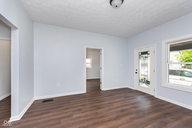 empty room with a wealth of natural light, dark hardwood / wood-style floors, and a textured ceiling