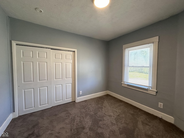 unfurnished bedroom with a textured ceiling, a closet, and dark carpet