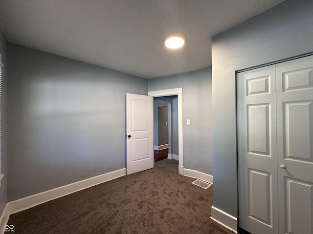 unfurnished bedroom featuring dark carpet and a closet