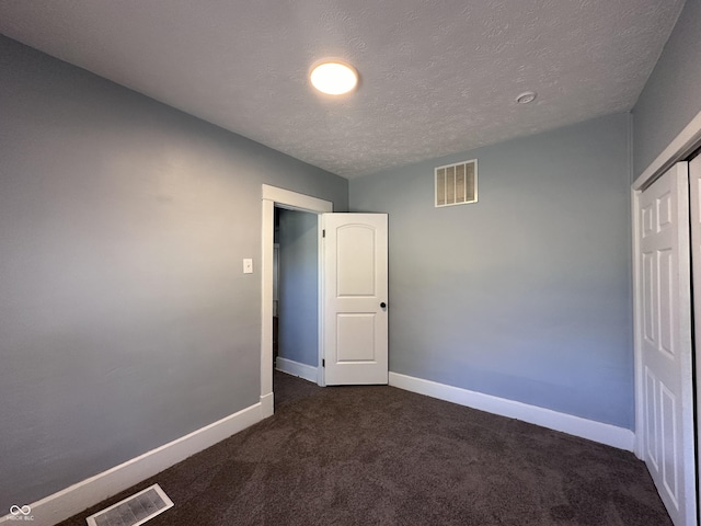 unfurnished bedroom with a textured ceiling, a closet, and dark carpet