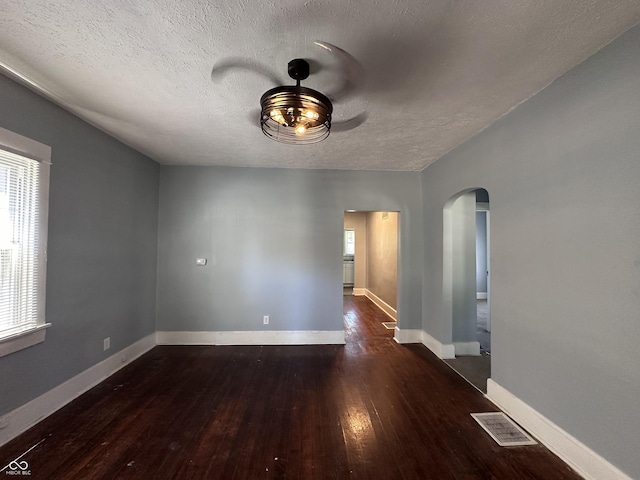 empty room with a textured ceiling, dark hardwood / wood-style floors, and a healthy amount of sunlight