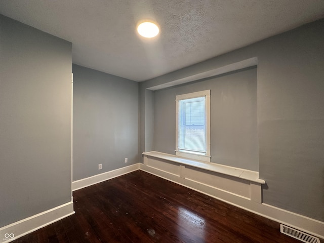 spare room featuring a textured ceiling and dark hardwood / wood-style floors