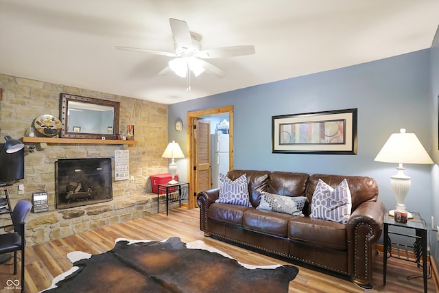 living room with a stone fireplace, ceiling fan, and wood-type flooring