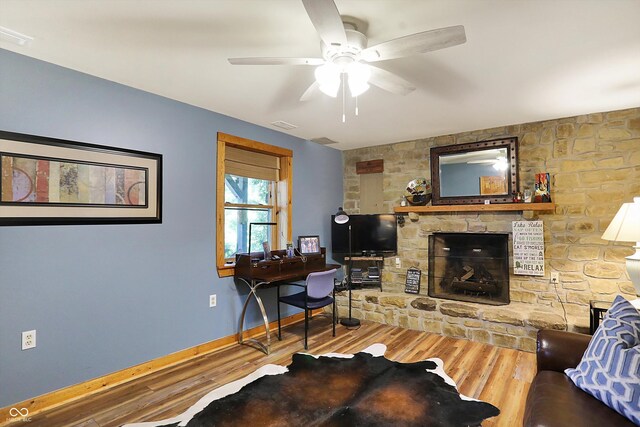 living room featuring a stone fireplace, hardwood / wood-style flooring, and ceiling fan