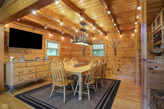 dining room with hardwood / wood-style floors, wooden walls, a healthy amount of sunlight, and beam ceiling