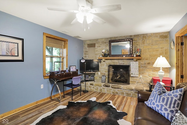 living room featuring a stone fireplace, hardwood / wood-style floors, and ceiling fan