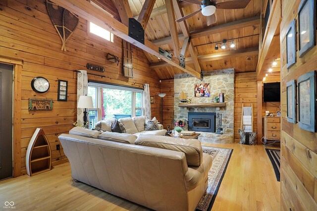 living room featuring light hardwood / wood-style flooring, wooden walls, ceiling fan, wooden ceiling, and a stone fireplace