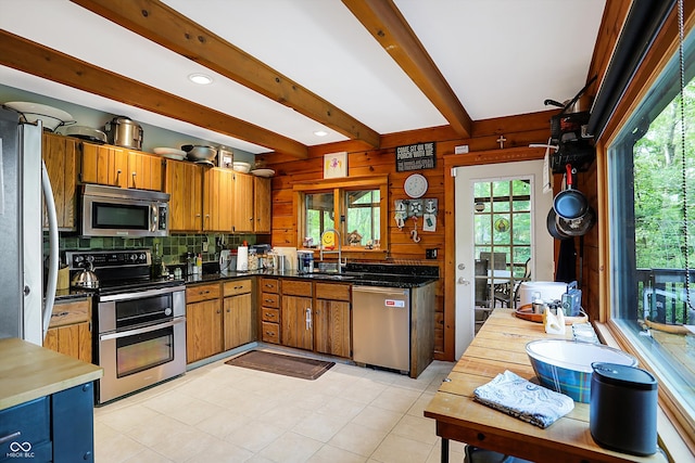 kitchen with beam ceiling, light tile patterned floors, wood walls, stainless steel appliances, and sink