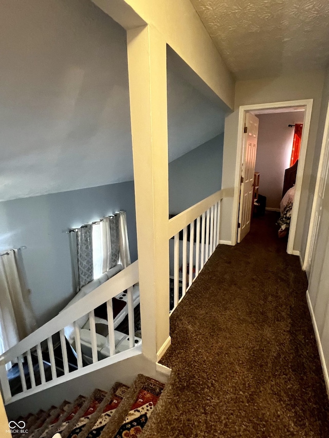 hall with dark carpet and a textured ceiling