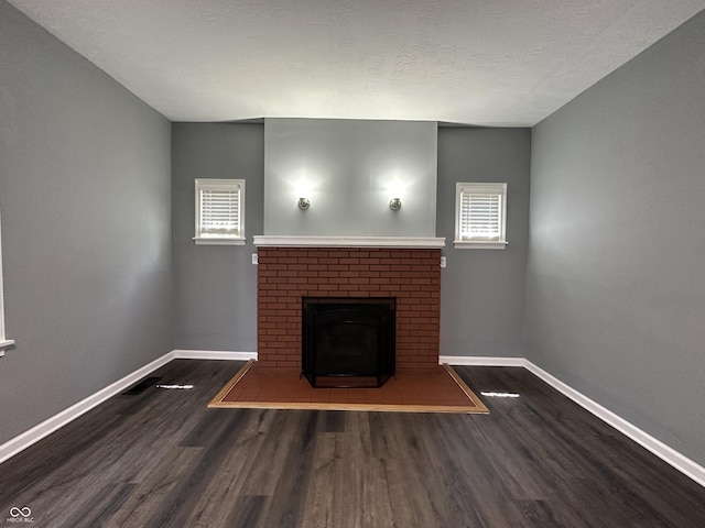 unfurnished living room featuring dark hardwood / wood-style floors, a brick fireplace, and a textured ceiling