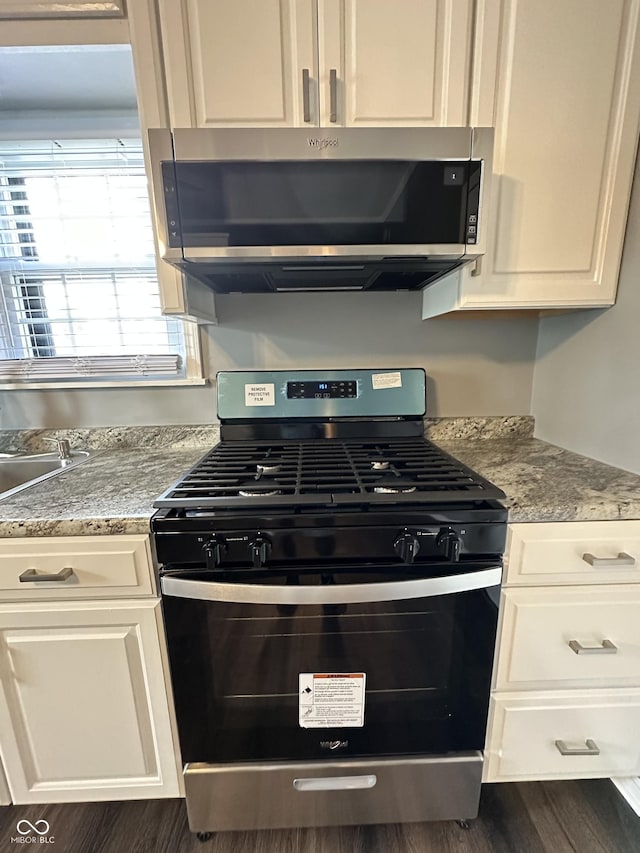 kitchen featuring light stone counters, black range with gas stovetop, dark hardwood / wood-style flooring, and white cabinets