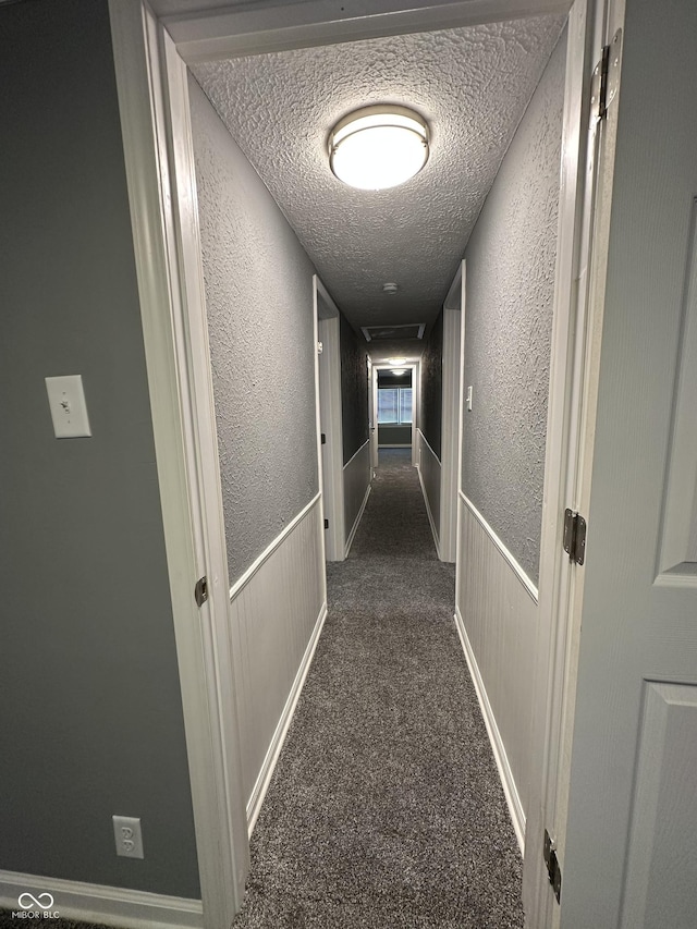 hallway featuring a textured ceiling and dark colored carpet