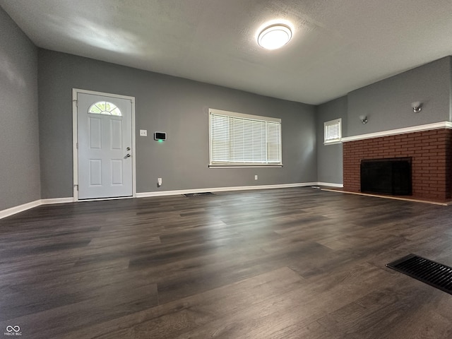 unfurnished living room with dark wood-type flooring, a wealth of natural light, a textured ceiling, and a fireplace