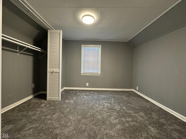 unfurnished bedroom featuring crown molding, vaulted ceiling, a closet, and dark colored carpet