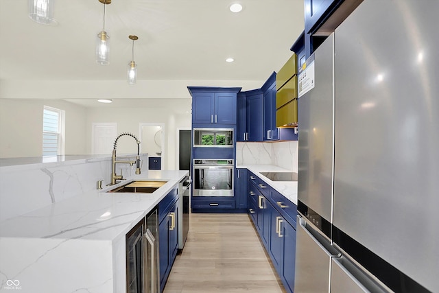 1218 Orange St, Indianapolis, IN 46203 - kitchen featuring stainless steel appliances, a sink, blue cabinets, light wood-style flooring, and decorative backsplash