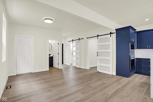 1218 Orange St, Indianapolis, IN 46203 - unfurnished living room featuring a barn door, light wood-type flooring, baseboards, and recessed lighting