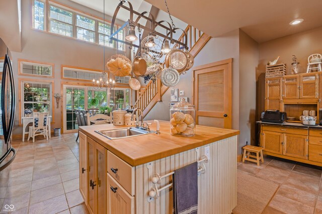 kitchen featuring a towering ceiling, an island with sink, sink, butcher block counters, and an inviting chandelier