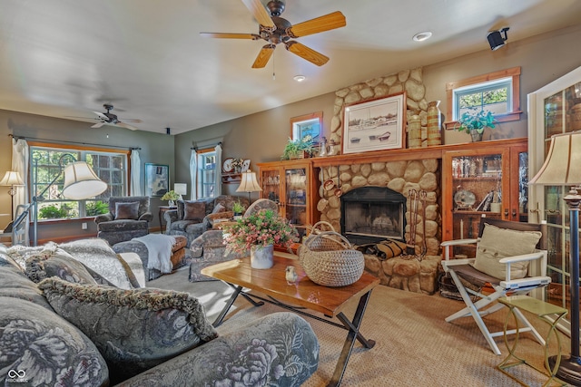 living room featuring ceiling fan, a stone fireplace, and a wealth of natural light