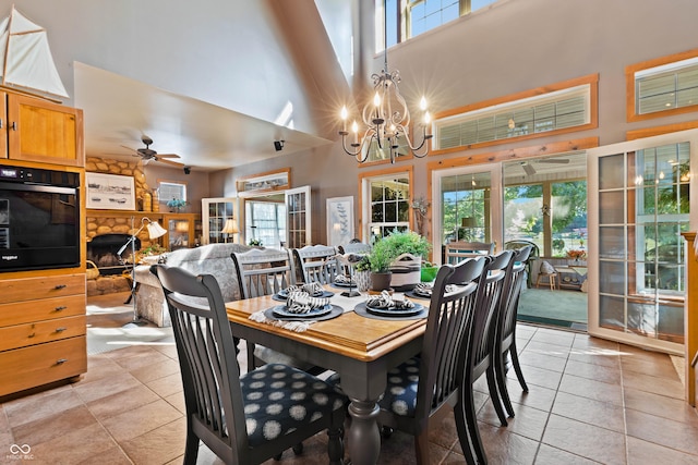 dining room with light tile patterned floors, ceiling fan with notable chandelier, a healthy amount of sunlight, and a high ceiling