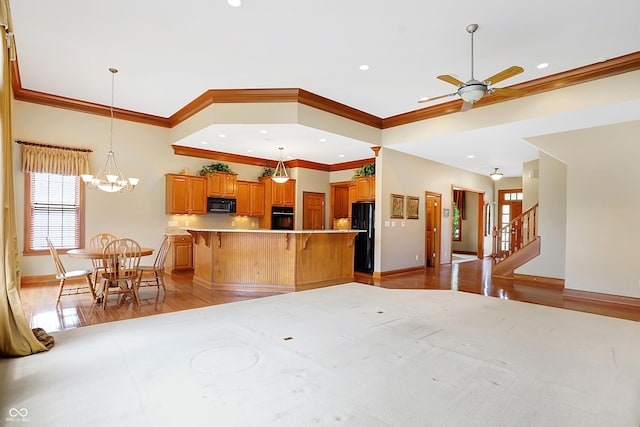 kitchen with a center island, crown molding, black appliances, ceiling fan with notable chandelier, and light wood-type flooring