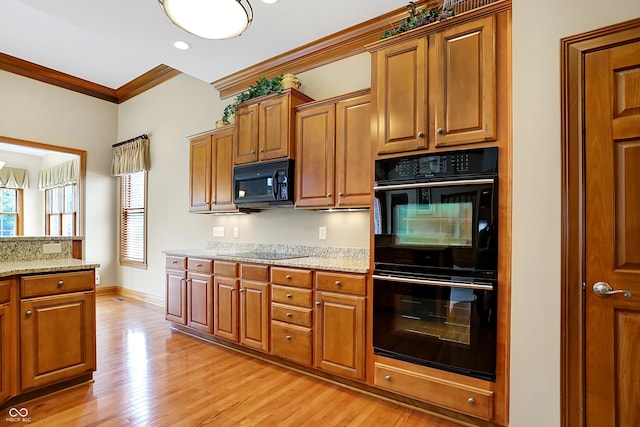 kitchen featuring light stone counters, crown molding, black appliances, and light wood-type flooring