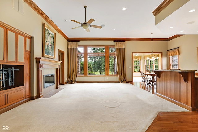 unfurnished living room featuring ceiling fan with notable chandelier, light colored carpet, ornamental molding, and a tiled fireplace