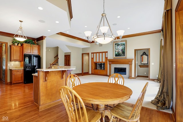 dining room with light hardwood / wood-style floors, crown molding, a tile fireplace, and a chandelier