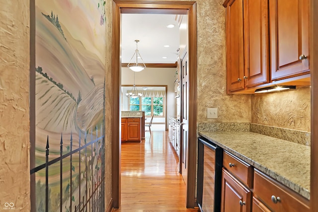 interior space featuring an inviting chandelier, wine cooler, ornamental molding, and light hardwood / wood-style floors