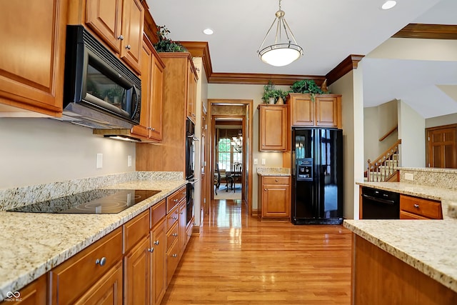 kitchen with light stone countertops, hanging light fixtures, light hardwood / wood-style floors, black appliances, and ornamental molding