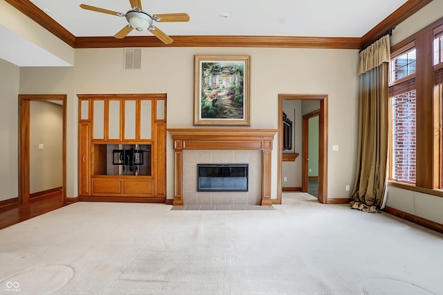 unfurnished living room with a tiled fireplace, crown molding, ceiling fan, and light colored carpet