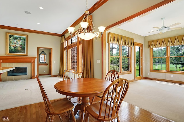 dining room with ceiling fan with notable chandelier, light hardwood / wood-style flooring, crown molding, and a tiled fireplace