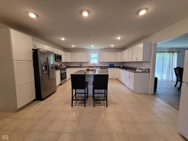 kitchen featuring a kitchen island, a textured ceiling, white cabinetry, stainless steel appliances, and a breakfast bar