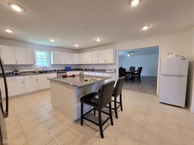 kitchen with a kitchen island, a kitchen breakfast bar, white cabinetry, dark stone countertops, and white refrigerator