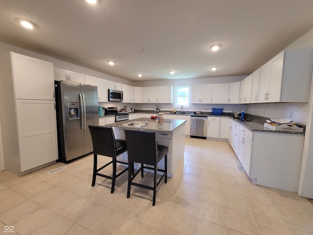 kitchen featuring a kitchen breakfast bar, stainless steel appliances, dark stone counters, a center island, and white cabinetry