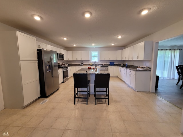 kitchen with a kitchen breakfast bar, sink, a center island, white cabinets, and appliances with stainless steel finishes