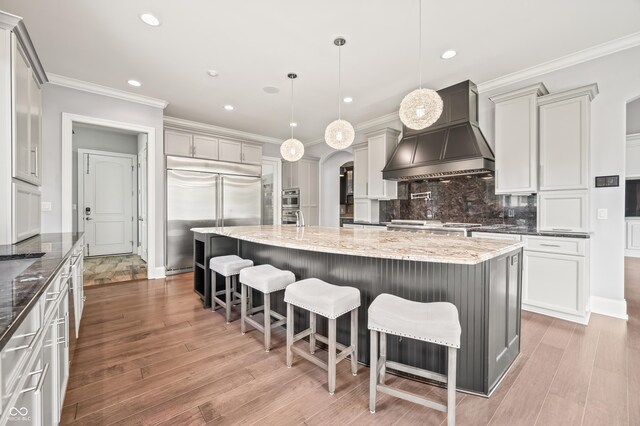 kitchen with stainless steel appliances, premium range hood, light hardwood / wood-style flooring, and a kitchen island