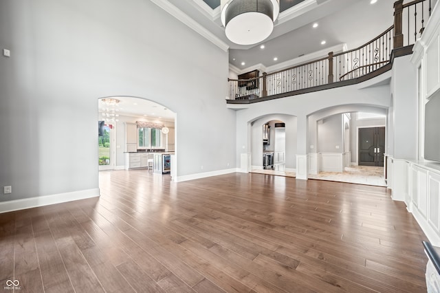 unfurnished living room with an inviting chandelier, a high ceiling, beverage cooler, hardwood / wood-style flooring, and ornamental molding