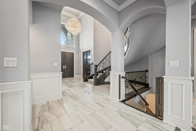 tiled entryway featuring a notable chandelier, crown molding, and a high ceiling