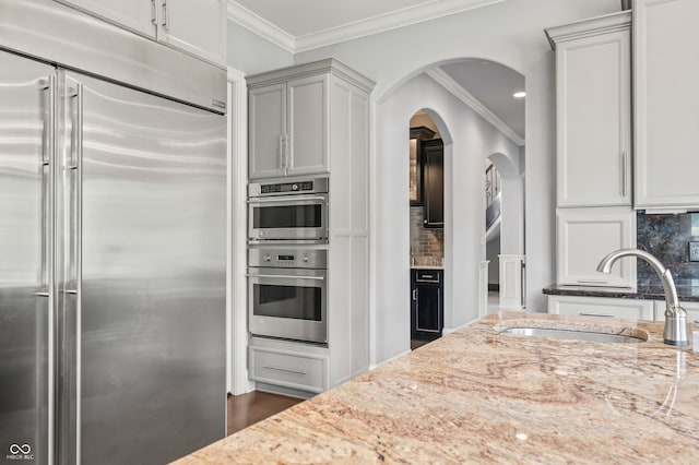 kitchen with decorative backsplash, sink, light stone counters, appliances with stainless steel finishes, and dark wood-type flooring