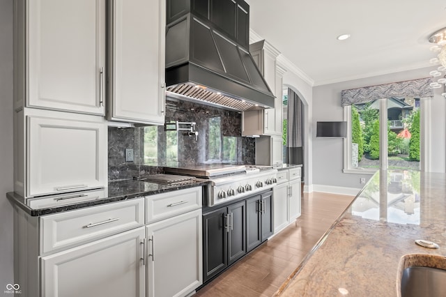 kitchen with dark stone countertops, crown molding, light hardwood / wood-style flooring, backsplash, and premium range hood