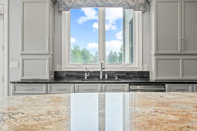 kitchen featuring stainless steel dishwasher, sink, and light stone counters