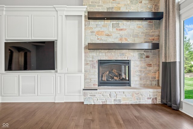 unfurnished living room featuring a stone fireplace, plenty of natural light, and dark wood-type flooring