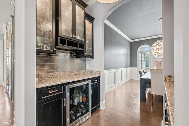 kitchen with hardwood / wood-style floors, light stone counters, decorative backsplash, crown molding, and beverage cooler