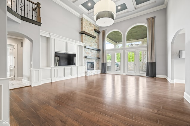 unfurnished living room with a stone fireplace, dark hardwood / wood-style floors, a towering ceiling, and coffered ceiling