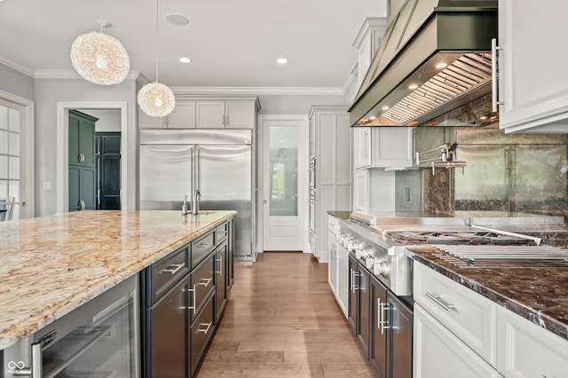 kitchen with crown molding, dark stone countertops, custom range hood, light hardwood / wood-style floors, and appliances with stainless steel finishes