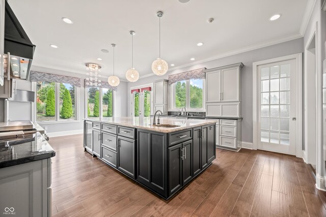 kitchen with hardwood / wood-style flooring, light stone countertops, sink, and an island with sink